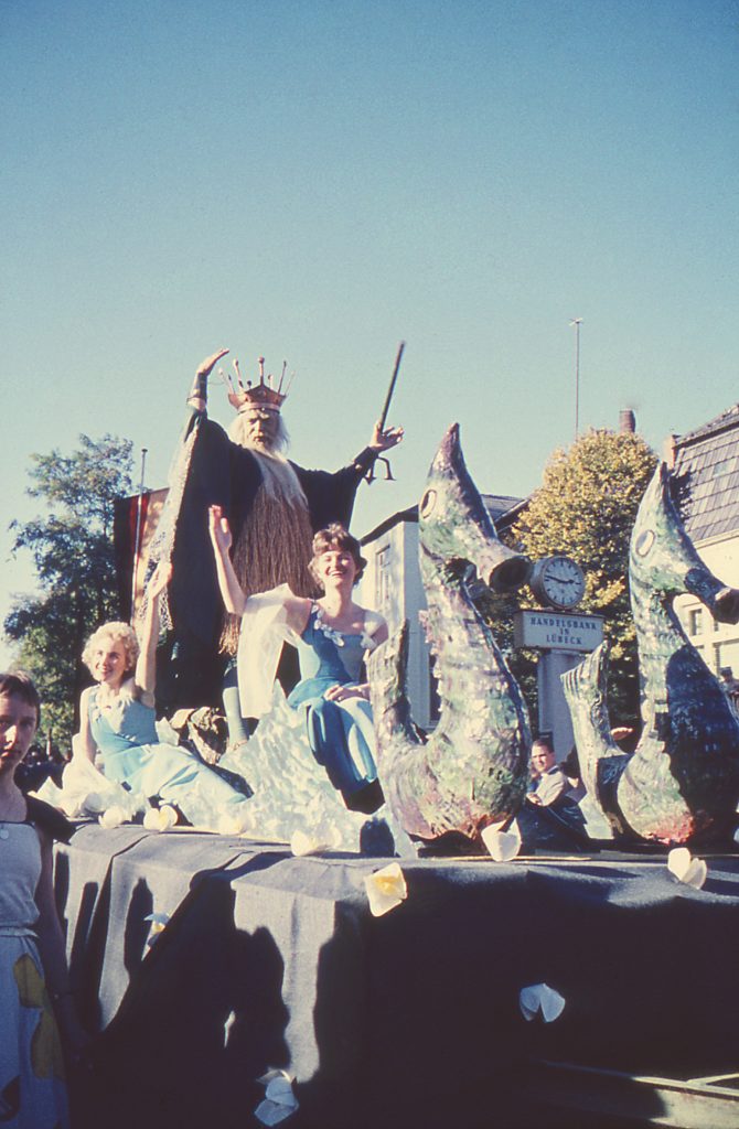 Reinfeld: Karpfenfest: Umzug: Paul-von-Schoenaich-Straße: Motto-Wagen mit Neptun, Nymphen und Seepferdchen: hinten Handelsbank in Lübeck mit Uhr: davor Zuschauer: hinten links Fahnenmasten und Bäume: 11. Oktober 1959