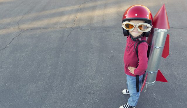 Young boy dressed in a red rocket suit on blacktop