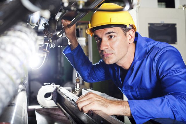Moderner Maschinenbediener mit gelben Helm und Overall